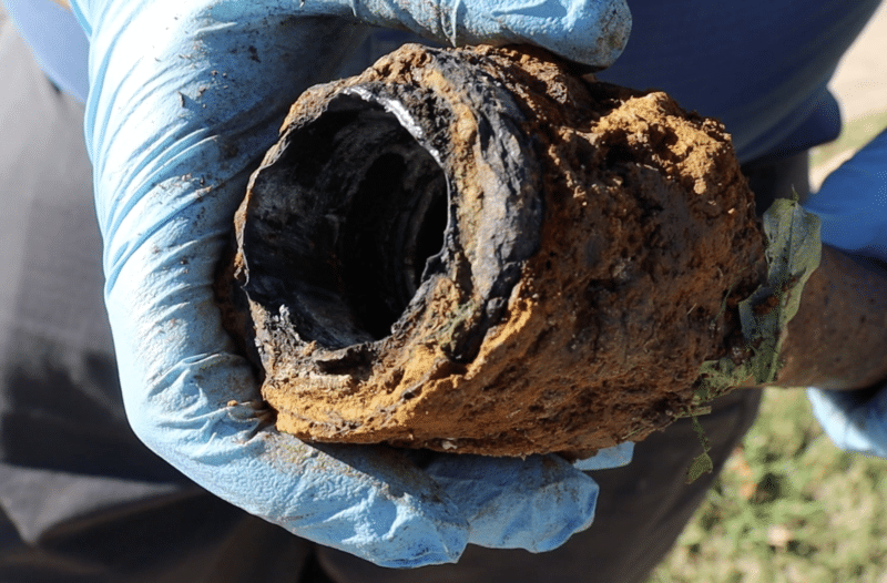 A plumber holding a cast iron pipe with channel rot.